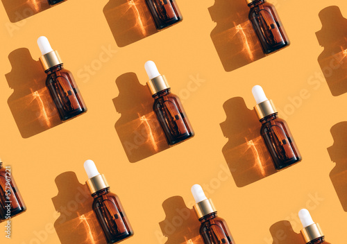 Pattern made of amber glass bottles with face serum or beauty oil with vitamin C over orange background. Beauty skin-care products with natural ingredients and fruit essence. Mockup