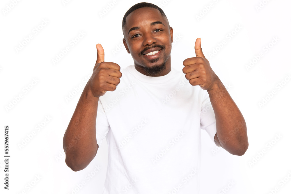 Pleased African American man showing thumbs up. Portrait of happy young male model with short hair in white T-shirt looking at camera, smiling, liking message. Social media, advertising concept Pleased African American man showing thumbs up. Portrait of happy young male model with short hair in white T-shirt looking at camera, smiling, liking message. Social media, advertising concept