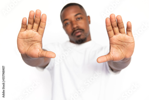 Dissatisfied African American man showing open palms. Hands of serious young male model with short hair and beard in white T-shirt looking at camera, showing stop sign. Restriction, refusal concept