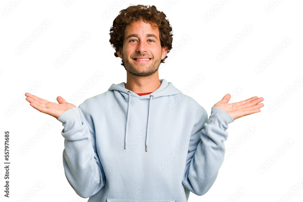 Young curly smart caucasian man cut out isolated makes scale with arms, feels happy and confident.
