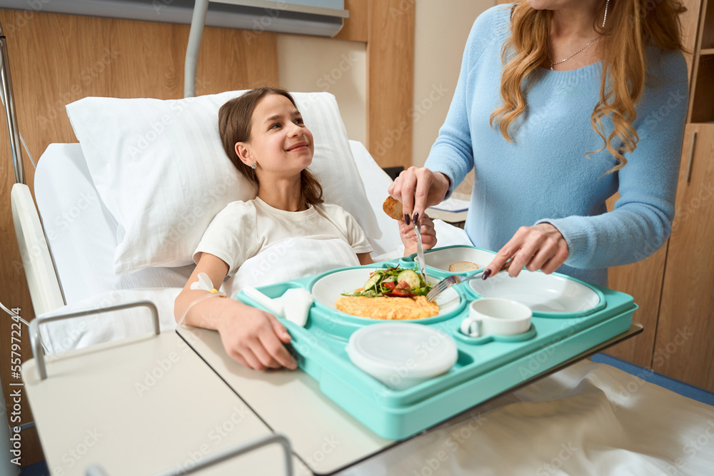 Mom feeds breakfast to a smiling daughter on hospital bed Mom feeds breakfast to a smiling daughter on hospital bed