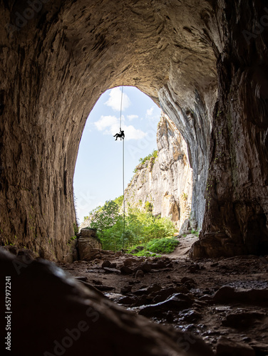 Climber hanging on a rope from a celiling of a giant cave boulder. Climbing in an overhang
