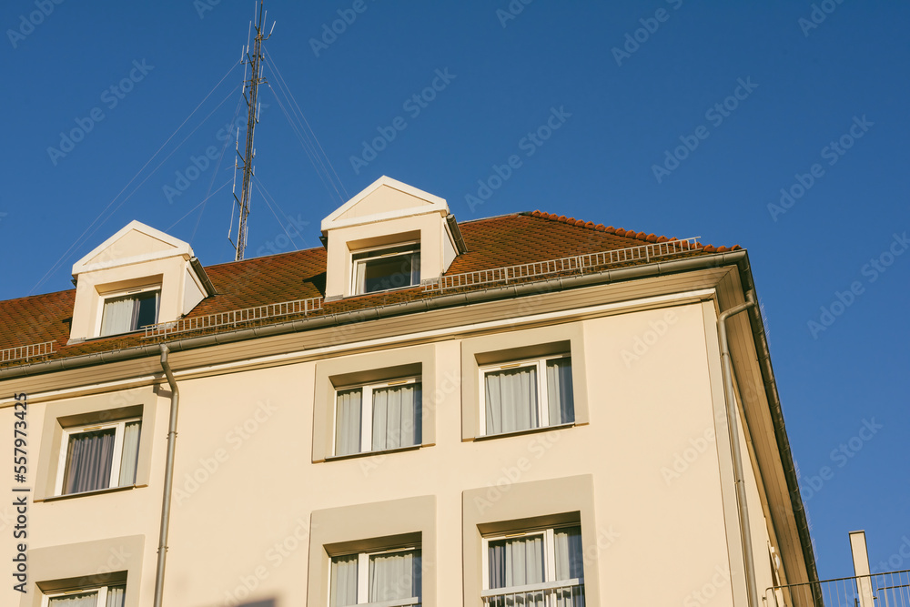 Large aerial antenna communication dish on the rooftop of apartment building with mansard type of apartments - clear blue sky in the background