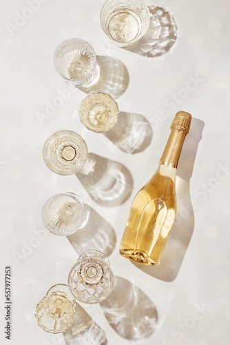 Fototapeta Flat lay with white sparkling wine bottle, set glasses wine with sunshine shadow and flare on light beige background