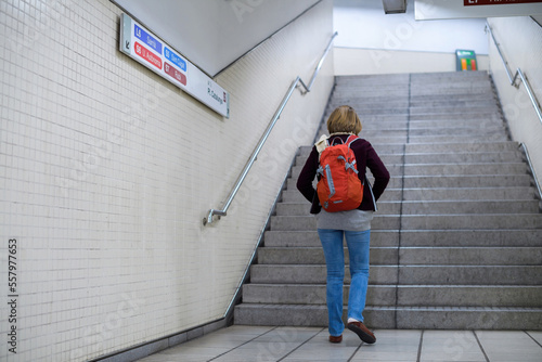 Rear view of single young woman with red backpack walking in the metro underground station with direction signs to diverse train on the wall © ifeelstock