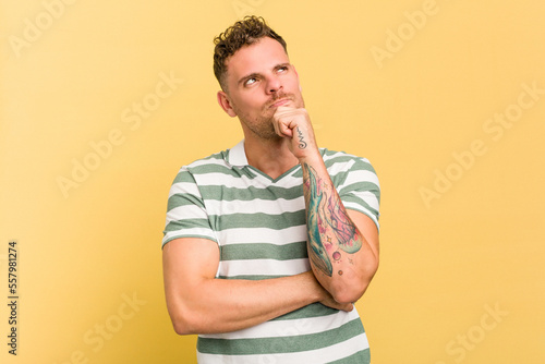 Fotografie, Tablou Young caucasian handsome man isolated on yellow background thinking and looking up, being reflective, contemplating, having a fantasy