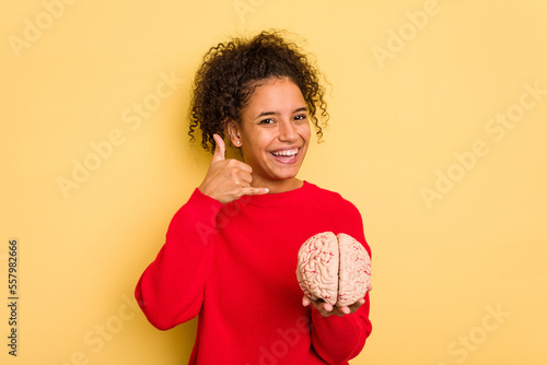 Young brazilian woman holding a brain model isolated showing a mobile phone call gesture with fingers.