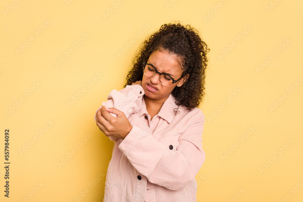 Young Brazilian curly hair cute woman isolated on yellow background massaging elbow, suffering after a bad movement. Young Brazilian curly hair cute woman isolated on yellow background massaging elbow, suffering after a bad movement.