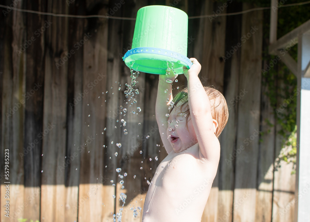 Caucasian toddler girl pouring water on her head from the green bucket