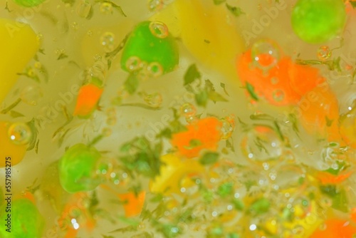 Close-up view of the vegetables with carrots, peas, cauliflower, corn, chopped potatoes and parsley in water background. Texture of boiling soup vegetables. Flat design, top view. 