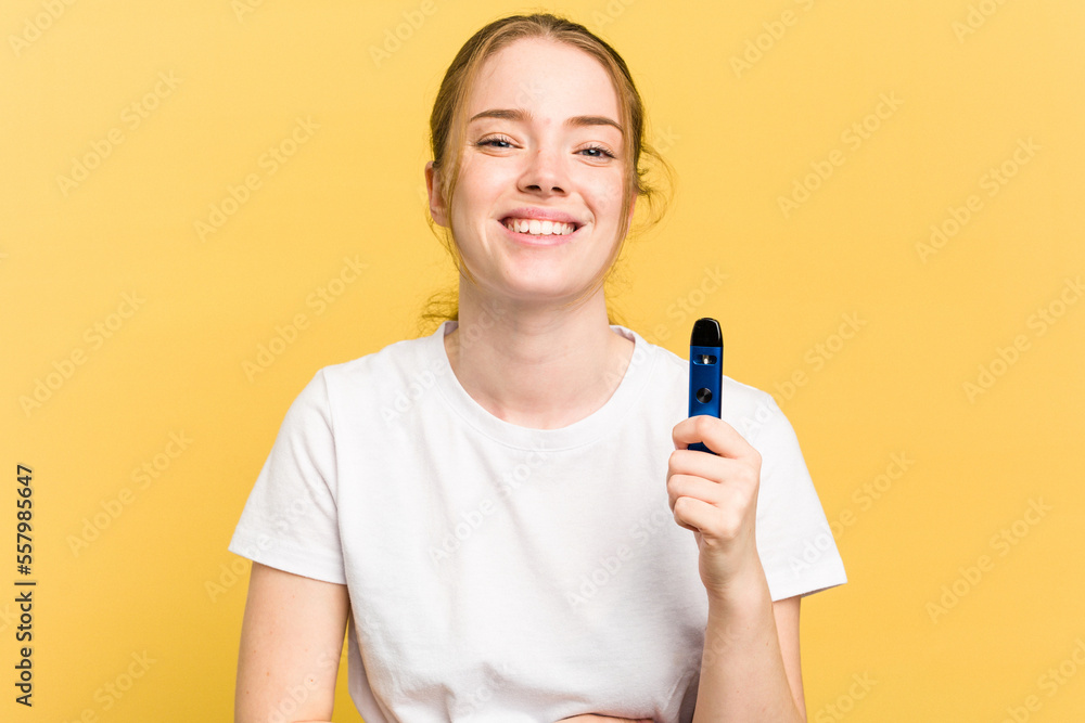 Young cute woman holding a vaper isolated on yellow background laughing and having fun. Young cute woman holding a vaper isolated on yellow background laughing and having fun.