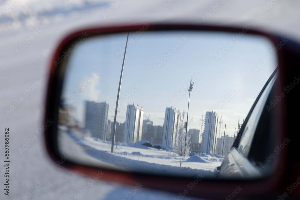 Reflection of the cityscape in the rear-view mirror of the car on a frosty winter day