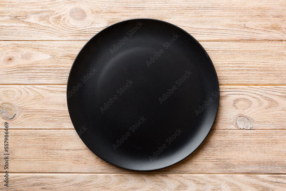 Top view of black plate on wooden background. Empty space for your design Top view of black plate on wooden background. Empty space for your design