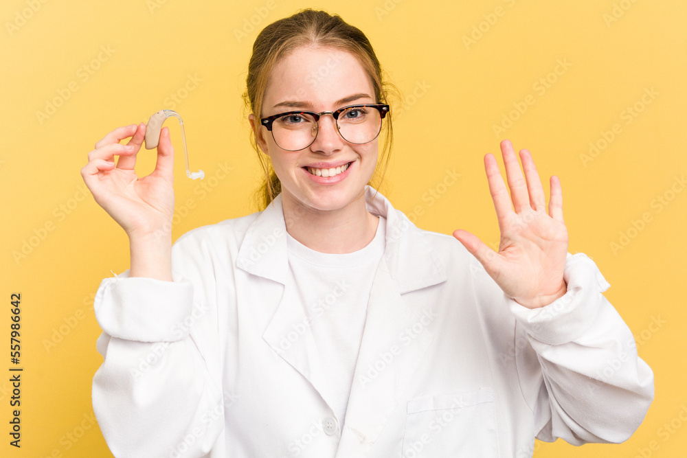 Young otorhinolaryngologist caucasian woman isolated on yellow background smiling cheerful showing number five with fingers. Young otorhinolaryngologist caucasian woman isolated on yellow background smiling cheerful showing number five with fingers.