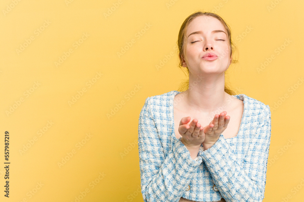 Young caucasian redhead woman isolated on yellow background folding lips and holding palms to send air kiss. Young caucasian redhead woman isolated on yellow background folding lips and holding palms to send air kiss.