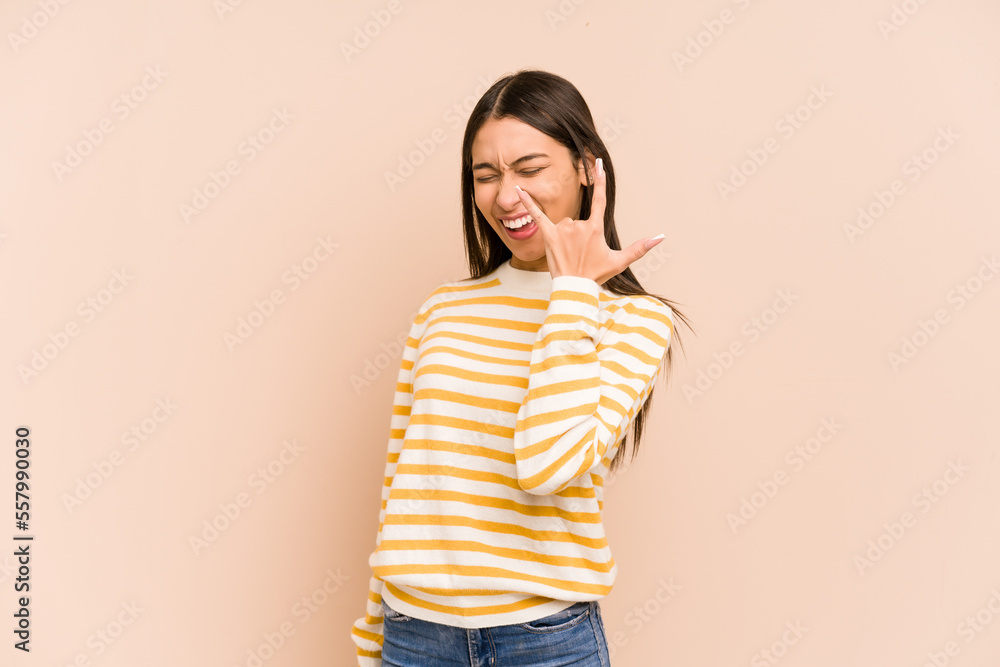 Young colombian woman isolated on beige background showing rock gesture with fingers Young colombian woman isolated on beige background showing rock gesture with fingers