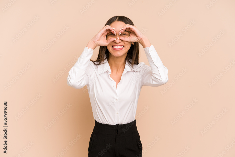 Young colombian woman isolated on beige background showing okay sign over eyes Young colombian woman isolated on beige background showing okay sign over eyes