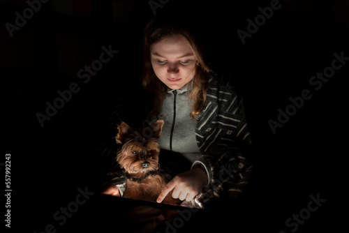 Blackout. A girl with a small dog uses a tablet pc in a dark room