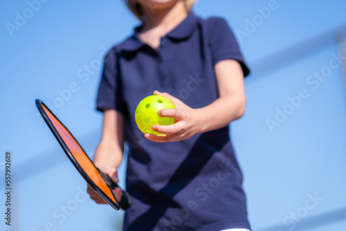 Laughing boy and girl playing pickleball game, hitting pickleball yellow ball with paddle, outdoor sport leisure kids activity.