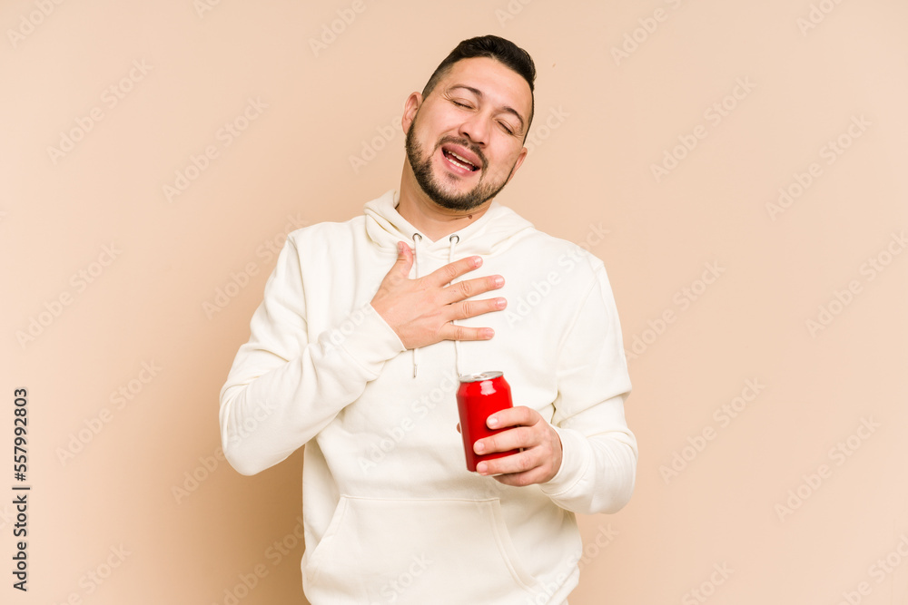 Young latin man holding a cola refreshment isolated laughs out loudly keeping hand on chest. Young latin man holding a cola refreshment isolated laughs out loudly keeping hand on chest.