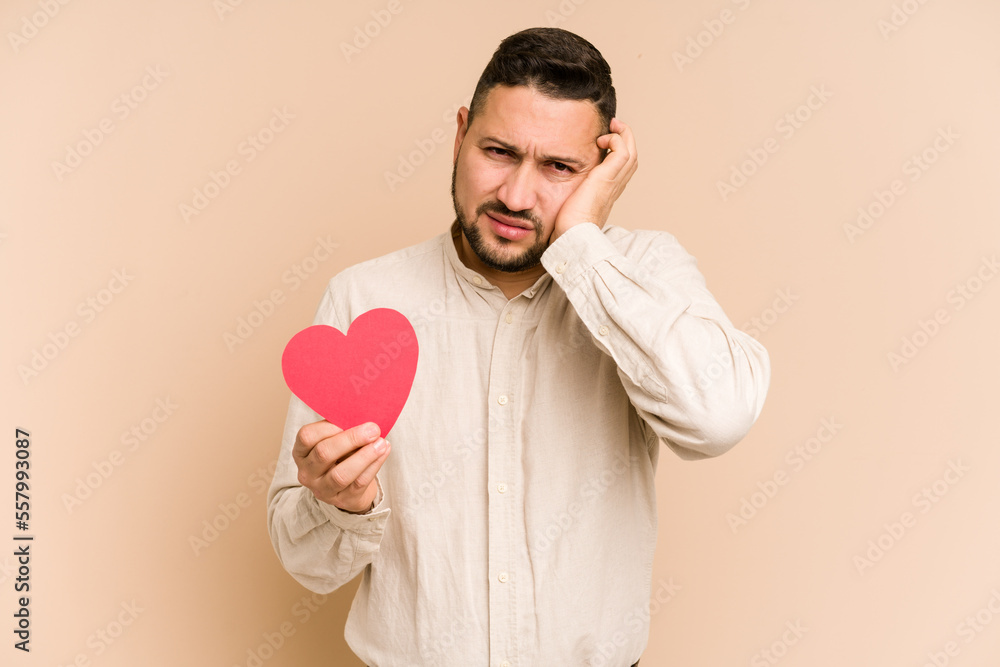 Adult latin man holding a red heart isolated covering ears with hands. Adult latin man holding a red heart isolated covering ears with hands.