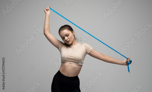 Attractive brunette woman in sportswear holding a blue measuring tape. Weight loss and diet concepts. Health care and healthy nutrition. Perfect slim body.