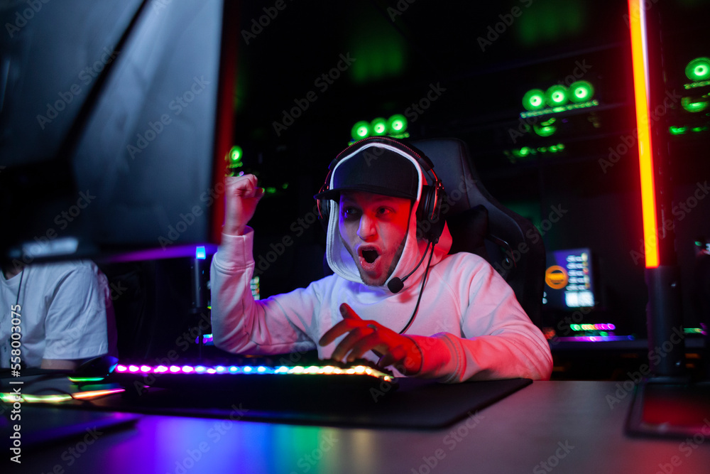 emotional guy gamer in headphones sits in a computer club and plays a computer game, a man shouts at the monitor emotional guy gamer in headphones sits in a computer club and plays a computer game, a man shouts at the monitor