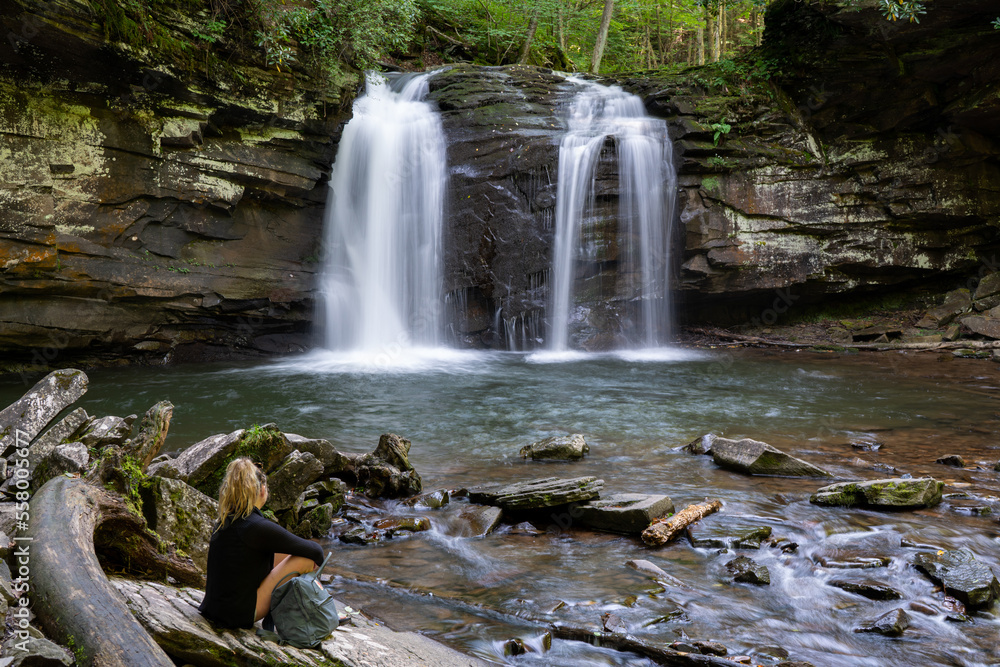 Obraz premium A woman sits by Seneca Creek below Seneca Falls in the Spruce Knob/Seneca Rocks National Recreation Area, part of the Monongahela National Forest in West Virginia.