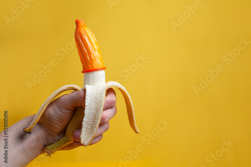 hand holds a banana with a condom, a contraceptive dressed on a sexualized banana on a yellow background