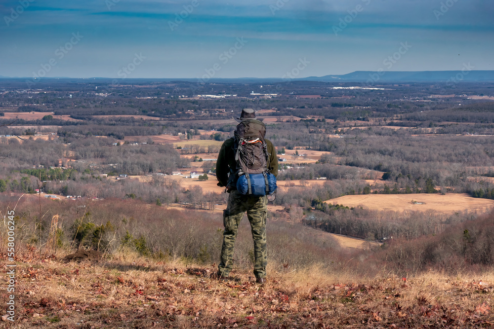 A man on a mountain looking from a cliff over the valley with a backpack filled with camping gear. At Keith Springs Mountain in Franklin County Tennessee USA.
