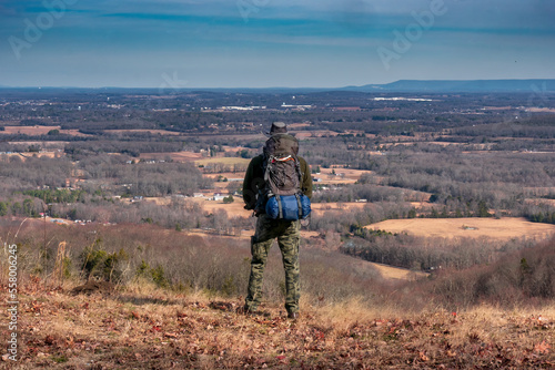 A man on a mountain looking from a cliff over the valley with a backpack filled with camping gear. At Keith Springs Mountain in Franklin County Tennessee USA.