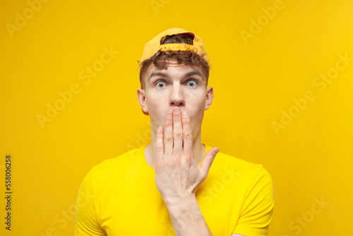 curly guy in shock covered his mouth with his hand and wonders on a yellow background