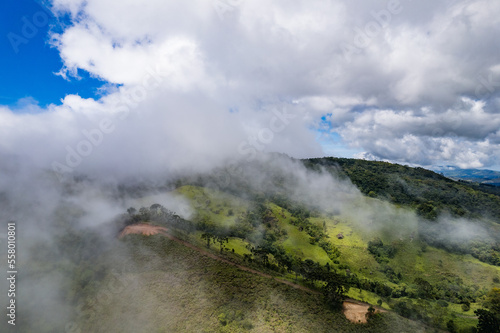 Aerial image of mountains with low clouds covering part of the landscape. Heavy clouds  green vegetation and very blue sky. Mist and white clouds.
