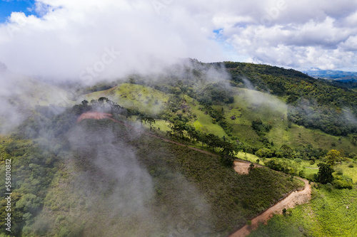 Aerial image of mountains with low clouds covering part of the landscape. Heavy clouds, green vegetation and very blue sky. Mist and white clouds.