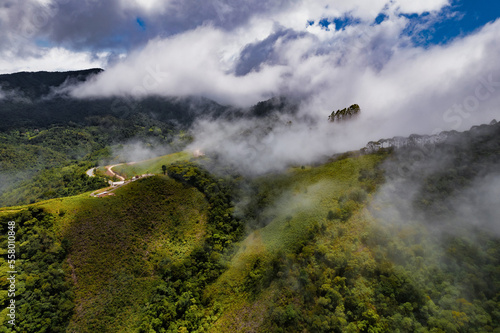 Aerial image of mountains with low clouds covering part of the landscape. Heavy clouds, green vegetation and very blue sky. Mist and white clouds.