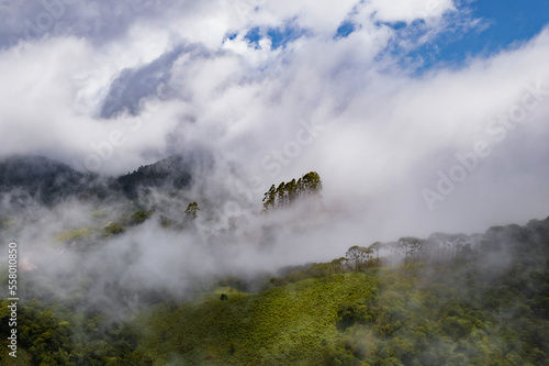 Aerial image of mountains with low clouds covering part of the landscape. Heavy clouds, green vegetation and very blue sky. Mist and white clouds. © Paulo