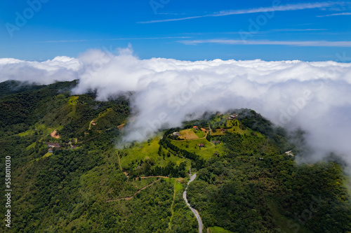 Aerial image of mountains with low clouds covering part of the landscape. Heavy clouds, green vegetation and very blue sky. Mist and white clouds.