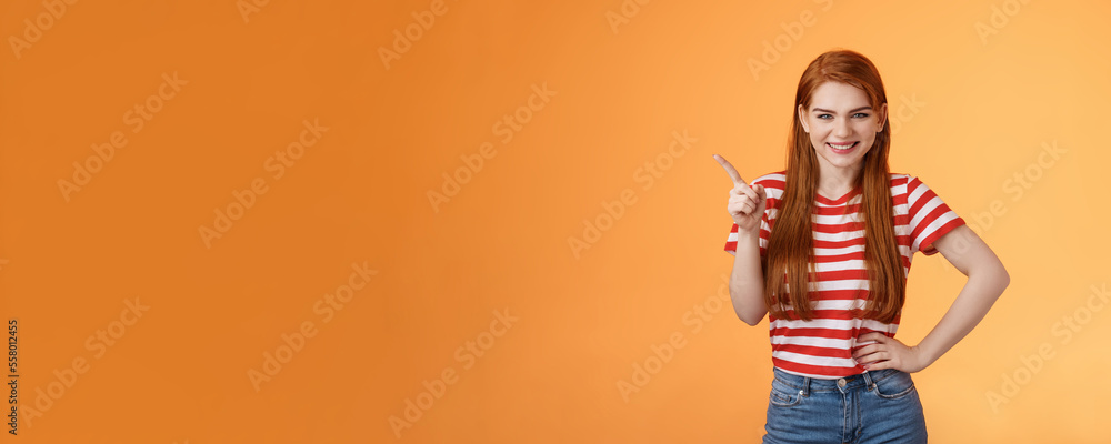 Cheerful sly redhead girlfriend have something interesting on mind, squinting cunning joyful smile, hold hand waist confident pose, pointing upper left corner give recommendation, orange background - obrazy, fototapety, plakaty 
