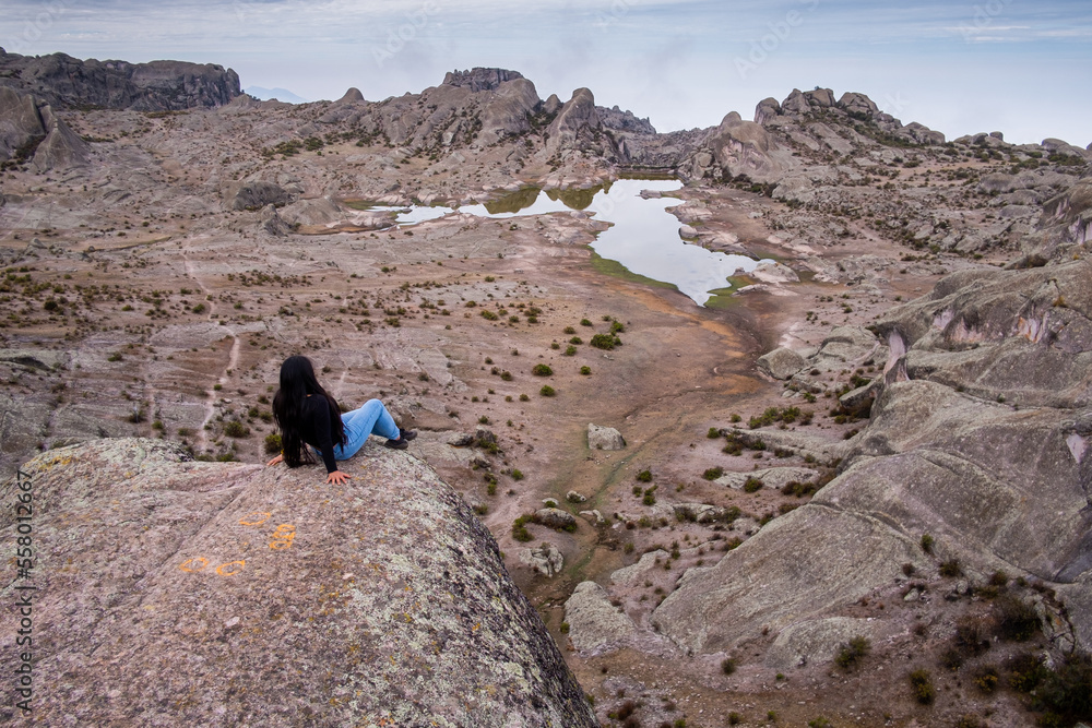latina woman lying on a rock, with a lagoon and a valley of rocks in the background