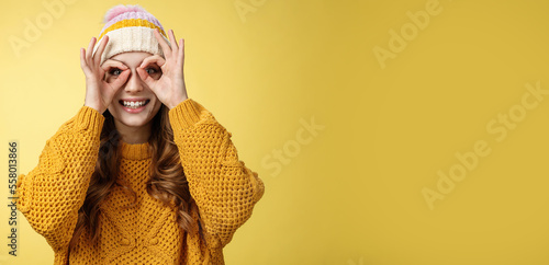 Surprised amused interested attractive young european woman wearing corduroy hat knitted sweater widen eyes curious show binocular glasses made fingers, smiling amazed, yellow background