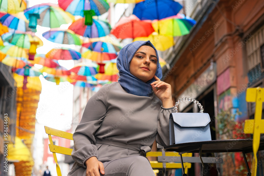 Girl in hijab, colorful umbrellas, sitting on chair. Young hijab girl poses for social media,