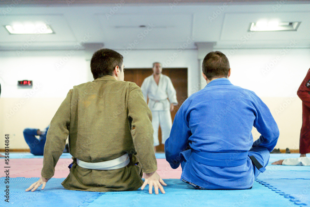 Three male jiujitsu trainees with their kimono on observing a combat in a closed environment. Three male jiujitsu trainees with their kimono on observing a combat in a closed environment.