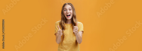 Excited girl expressed support and cheer raising thumbs up in approval and like gesture smiling optimistic and positive being amused with awesome idea standing pleased over orange background