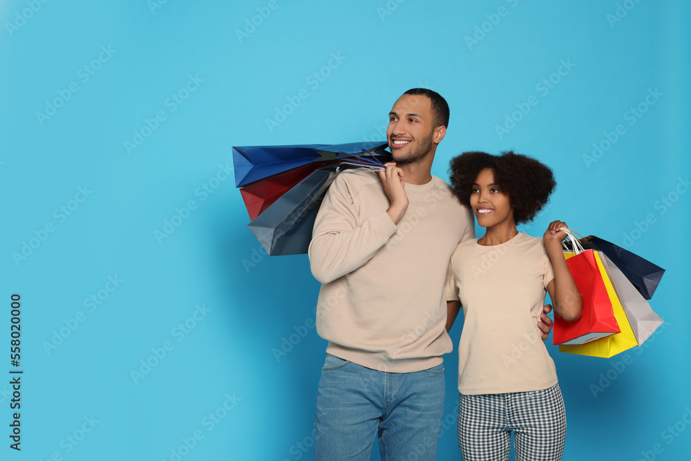 Happy African American couple with shopping bags on light blue background. Space for text Happy African American couple with shopping bags on light blue background. Space for text