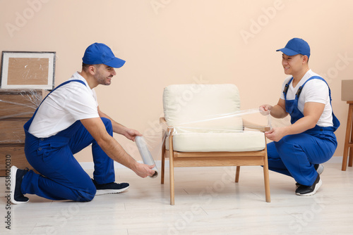 Workers wrapping armchair in stretch film indoors