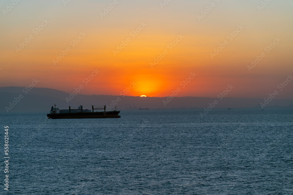 Just a sliver of the sun remains as it sets behind the desert dunes as a cargo ship sails along the Suez Canal, Egypt.