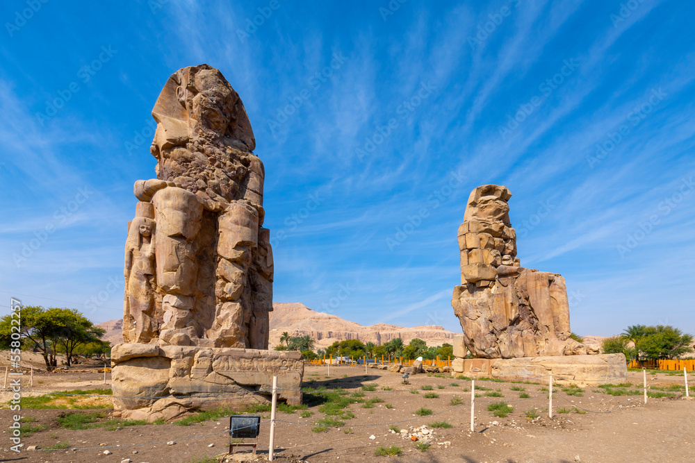 The ancient Egyptian Colossi of Memnon, two massive stone statues of the Pharaoh Amenhotep III, which stand at the front of the ruined Mortuary Temple of Amenhotep in Luxor, Egypt.