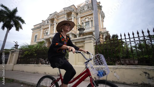 Laughing, happy, fun mature elderly woman in ethnic clothing and hat biking on the Central Avenue Paseo de Montejo with museums, restaurants, monuments and tourist attractions in Merida Yucatan Mexico photo