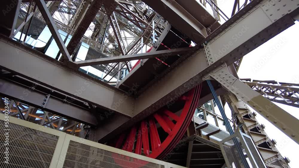 Red Gear Wheel Of Eiffel Tower Lift Rotating. Elevator Mechanism. closeup, low angle Red Gear Wheel Of Eiffel Tower Lift Rotating. Elevator Mechanism. closeup, low angle