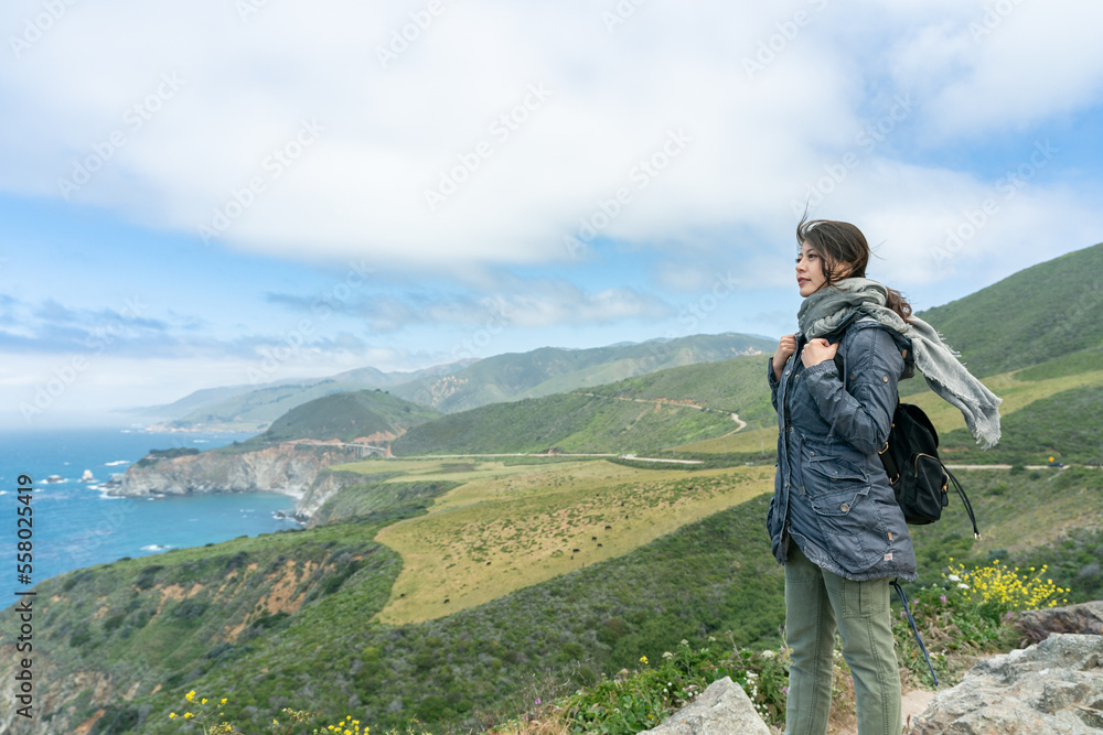 asian taiwanese woman backpacker overlooking scenic ocean and mountain view under blue sky while touring big sur in california usa